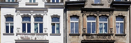 Zweistöckige Fassade mit Giebel, links frisch renoviert in Weiß, rechts unrenoviert mit sichtbarem Verwitterungsschmutz.