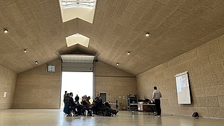 Ein weitläufiger Raum, in dem mehrere Personen um einen Tisch sitzen und sich austauschen.