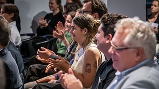 Veranstaltungsteilnehmende im Publikum applaudieren