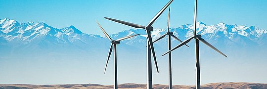 Windräder in der kasachischen Prärie, im Hintergrund Berge.