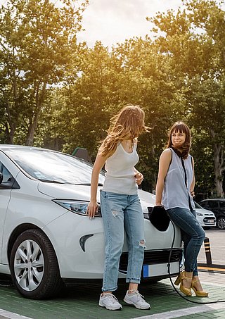 Zwei Frauen stützen sich auf Elektroauto an einer Ladesäule.  
