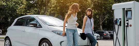 Zwei Frauen stützen sich auf Elektroauto an einer Ladesäule.