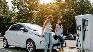 Zwei Frauen stützen sich auf Elektroauto an einer Ladesäule.  