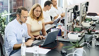 Zwei Teilnehmende der EnerCise Cyberübung III analysieren gemeinsam Daten auf einem Laptop, umgeben von technischer Ausrüstung wie Schalttafeln und Kabeln. Die Übung stärkt technische Fähigkeiten und das Bewusstsein für Cybersicherheit.