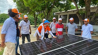 Auf dem Bild ist eine Gruppe von Menschen zu sehen, die um ein Solarmodul stehen.