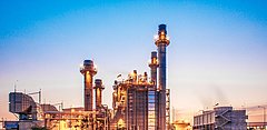 Industrieanlage mit zahlreichen Schornsteinen, beleuchtet im Dämmerlicht.