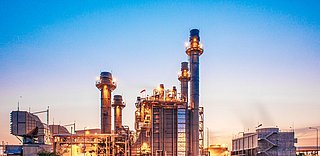 Industrieanlage mit zahlreichen Schornsteinen, beleuchtet im Dämmerlicht.