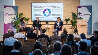 3 Personen auf einer Bühne vor Publikum, links und rechts Banner mit der Aufschrift "Future Energy Lab".
