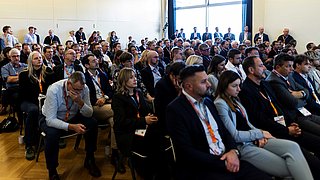 Blick ins Publikum, in dem viele Menschen sitzen und einige am Rand stehen.