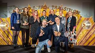 Gruppe von neun Personen mit Auszeichnungen posiert vor einer goldfarbenen Wand mit dem Schriftzug 'STARTUP ENERGY TRANSITION'.
