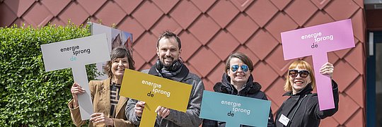 Vier Personen stehen vor einer Hauswand mit je einem Schild in der Hand. Aufschrift: energiesprong.de