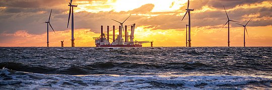 Offshore-Windpark mit Windrädern und einem Schiff bei Sonnenuntergang über dem Meer.