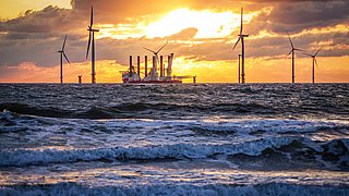 Offshore-Windpark mit Windrädern und einem Schiff bei Sonnenuntergang über dem Meer.