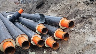 Schwarze Kunststoffrohre mit orangefarbenen Innenrohren liegen auf einem Erdhaufen auf einer Baustelle.