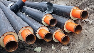 Schwarze Kunststoffrohre mit orangefarbenen Innenrohren liegen auf einem Erdhaufen auf einer Baustelle.