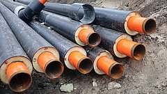 Schwarze Kunststoffrohre mit orangefarbenen Innenrohren liegen auf einem Erdhaufen auf einer Baustelle.