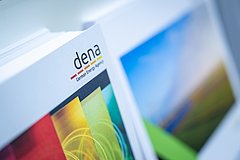 Zwei Stapel von Broschüren, eine mit dem Logo 'dena' und dem Text 'German Energy Agency'. Die andere zeigt eine Landschaftsaufnahme.
