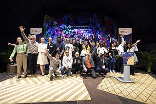 Gruppenfoto der Gewinner des SET Award 2023 auf Bühne mit buntem Hintergrund, einige Personen jubeln mit erhobenen Armen