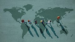 Sechs Personen gehen auf einer Weltkarte auf dem Boden und werfen lange Schatten