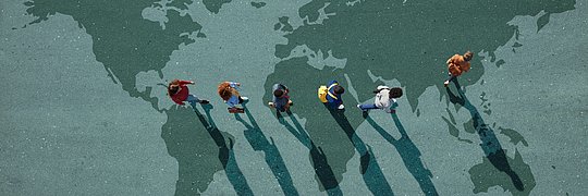 Sechs Personen gehen auf einer Weltkarte auf dem Boden und werfen lange Schatten