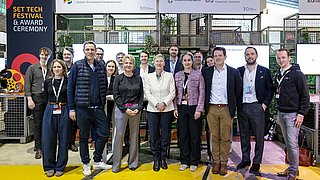 Gruppe von Menschen mit Ausweisen steht vor Messestand mit Bannern der Deutsch-Schwedischen Handelskammer und der Swedish Energy Agency auf gelbem Boden