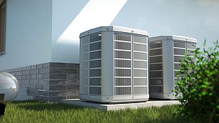 Zwei graue Klimaanlagen mit Gitterstruktur stehen nebeneinander auf einem Betonfundament, umgeben von grünem Gras.