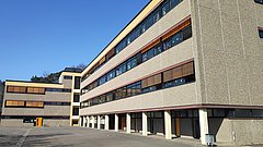 Mehrstöckiges Schulgebäude mit großen Fenstern und gelben Fensterläden unter klarem blauem Himmel