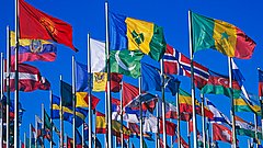 Mehrere Flaggen verschiedener Länder wehen an Fahnenmasten vor blauem Himmel