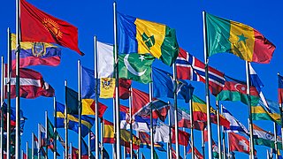 Mehrere Flaggen verschiedener Länder wehen an Fahnenmasten vor blauem Himmel