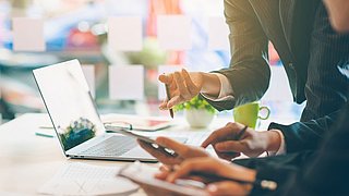 Auf dem Bild sieht man zwei Personen, die sich unterhalten und je einen Laptop halten. Man sieht von den Personen nur die Oberkörper. Die Gesichter sind nicht zu sehen.