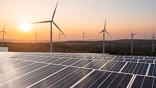 Solaranlagen und Windkraftanlagen vor einem Sonnenuntergang.