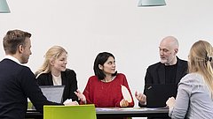 Eine Gruppe von Menschen sitzt um einen Tisch herum und arbeitet mit Laptops.