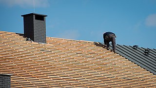 Ein Mann ist auf einem Dach beschäftigt, um Bau- oder Wartungsarbeiten durchzuführen.