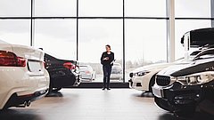 Full length of woman standing amidst cars in showroom