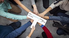 Mehrere Personen legen ihre Hände zusammen, eine hält ein Schild mit dem Text 'Wir engagieren uns bei energiesprong.de'