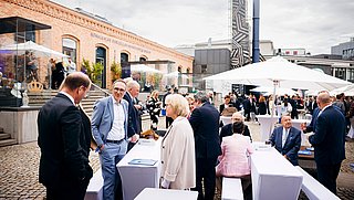 Auf dem Bild sind im Vordergrund Gäste bei der Jubiläumsfeier zu 25 Jahre dena in Berlin zu sehen. Links ist die Fassade der Königlichen Porzellanmanufaktur Berlin erkennbar.