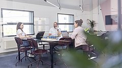 Drei Personen in einem modernen Büro, die an einem Tisch mit Laptops diskutieren.
