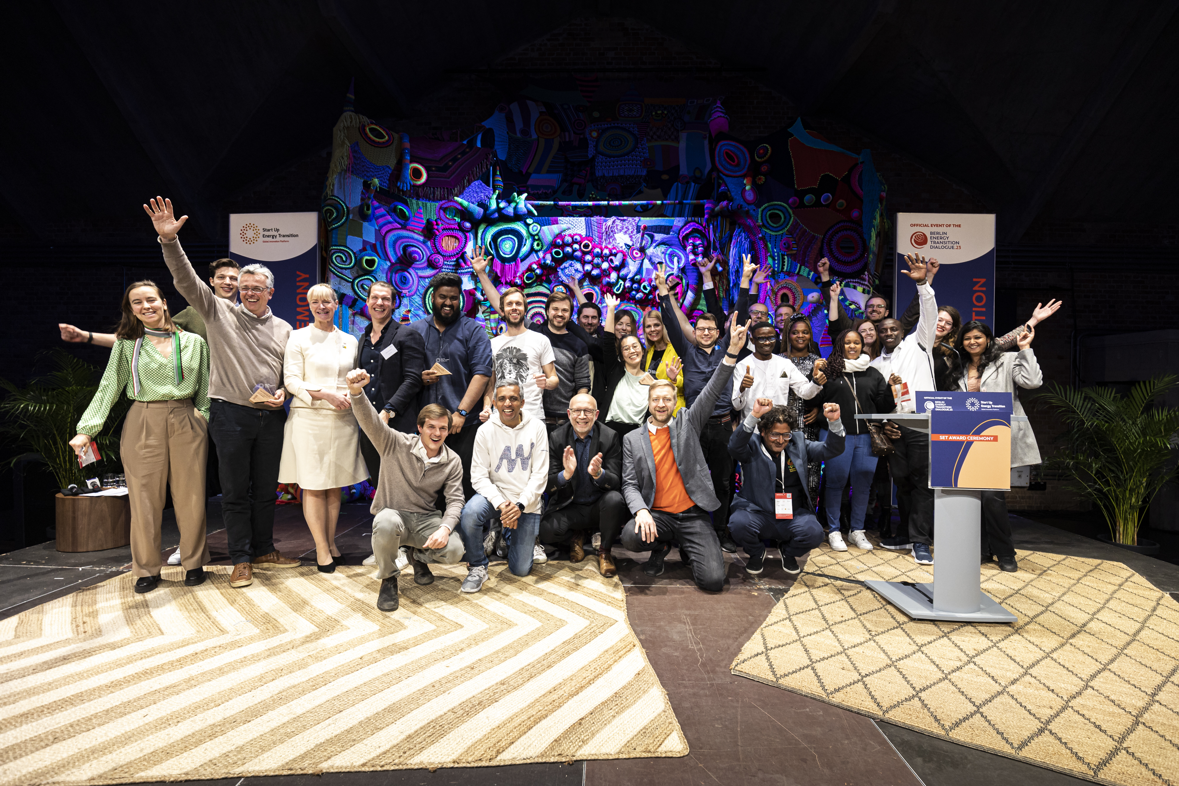 Gruppenfoto der Gewinner des SET Award 2023 auf Bühne mit buntem Hintergrund, einige Personen jubeln mit erhobenen Armen