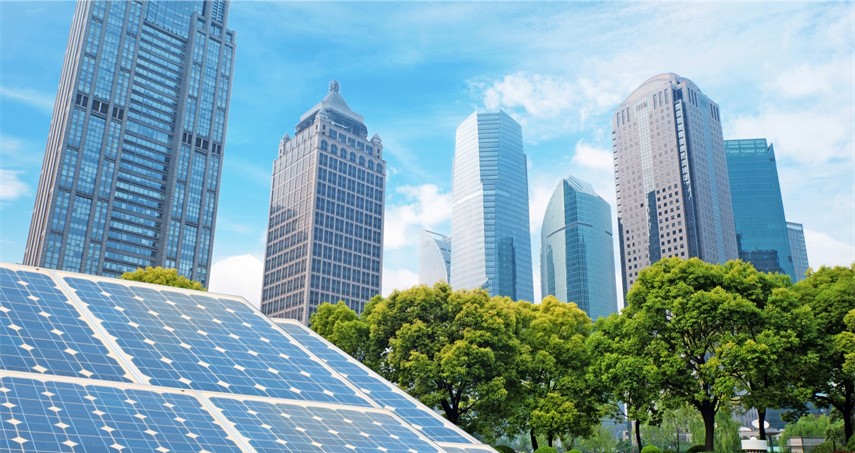 Solaranlage im Vordergrund mit blauen Solarpanelen, im Hintergrund moderne Wolkenkratzer und grüne Bäume unter blauem Himmel.