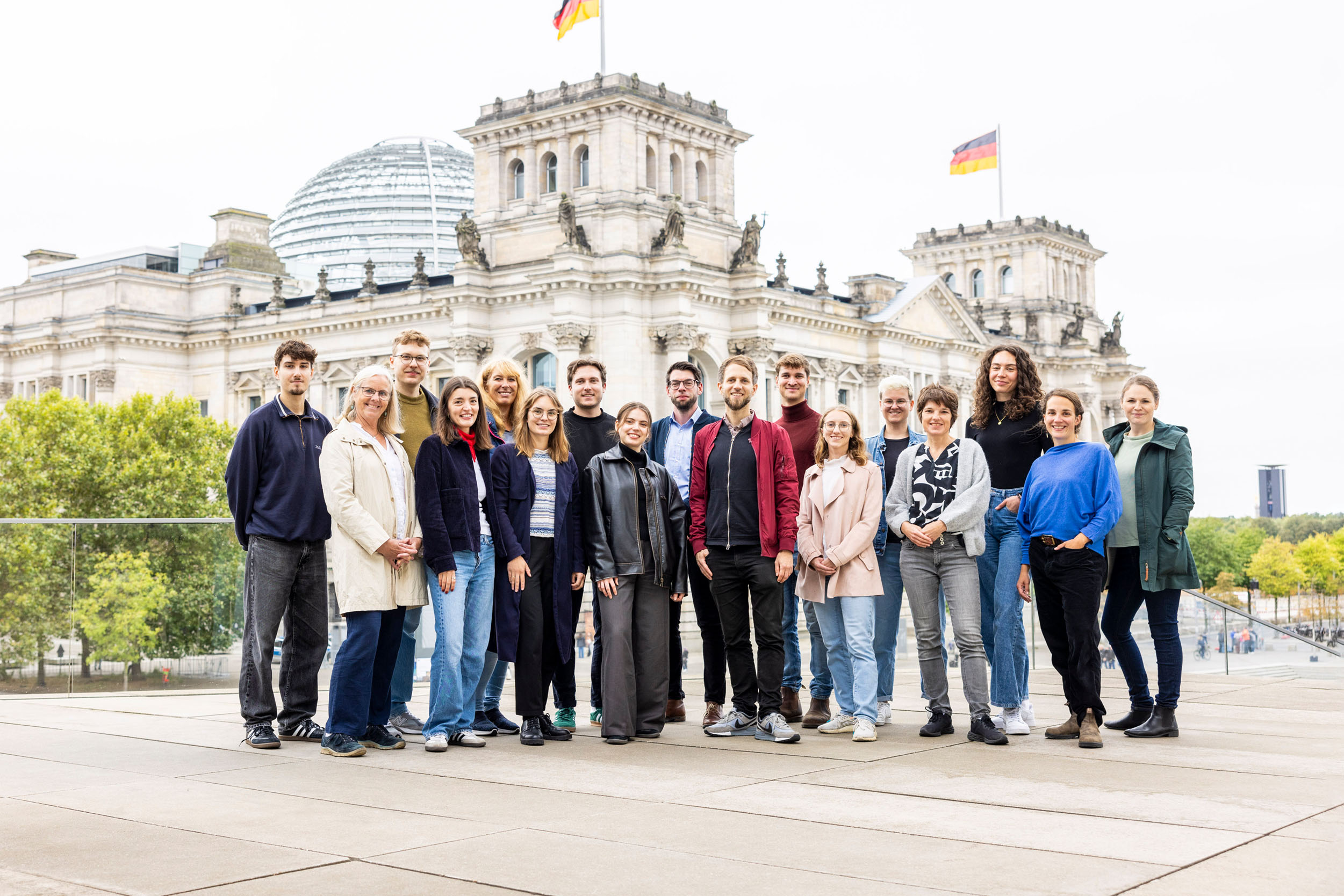 Gruppe von 17 Personen steht vor dem Reichstagsgebäude in Berlin mit zwei deutschen Flaggen auf den Türmen
