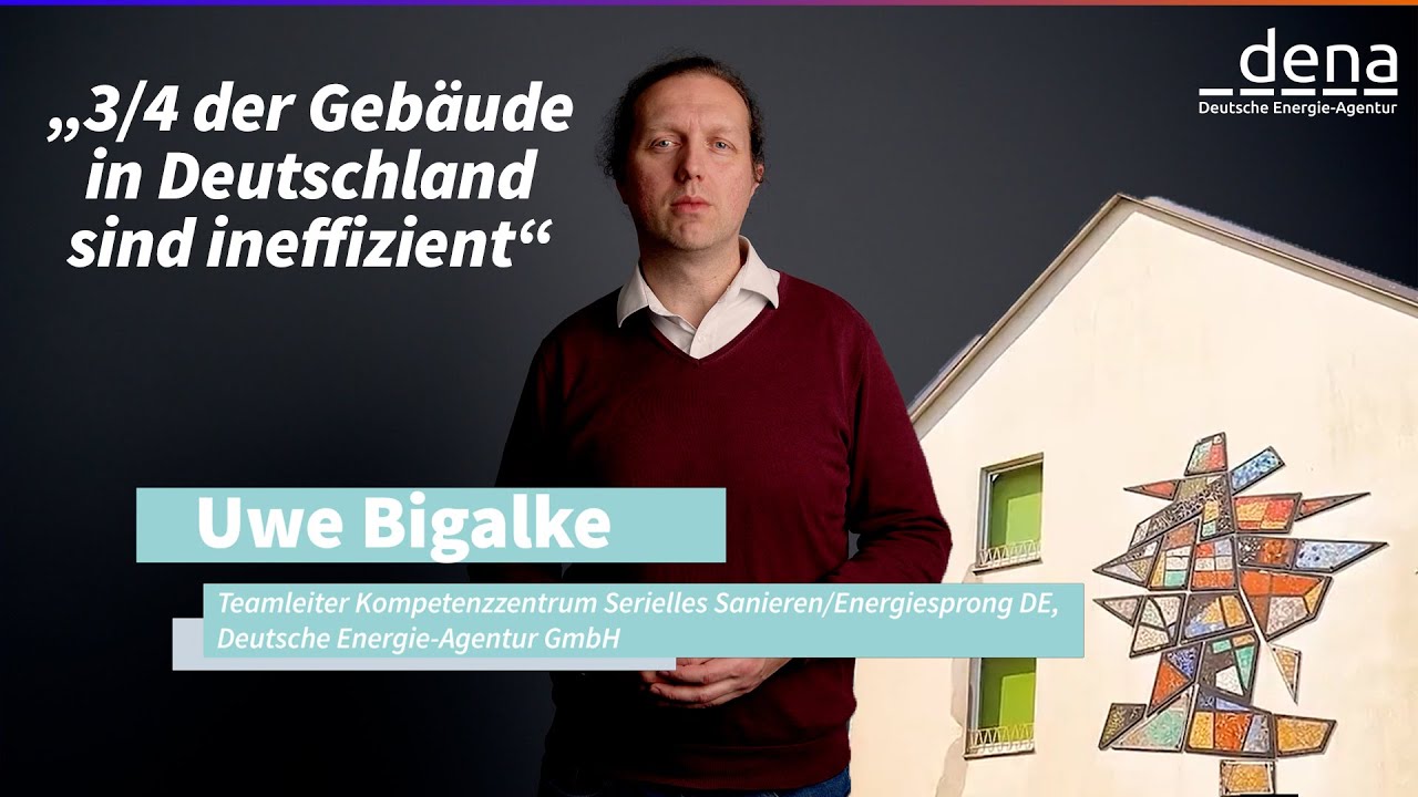 Eine Gruppe von Menschen beobachtet, wie ein großes vorgefertigtes Wandelement mit einem Kran an ein Gebäude montiert wird.